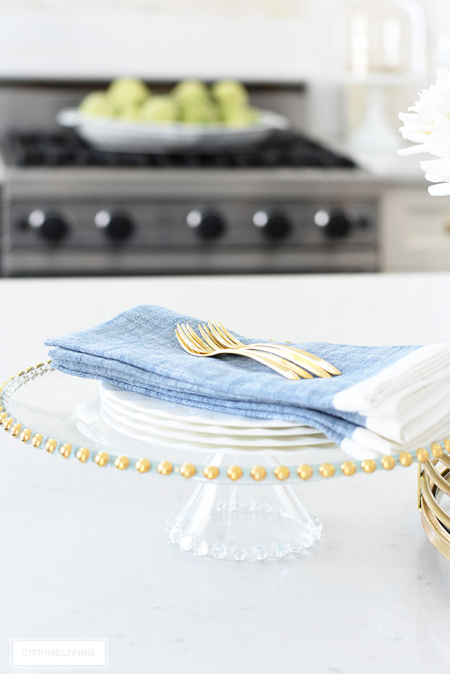 Spring kitchen decorating - elegant soft blue napkins, gold flatware displayed on a gold beaded cake stand.