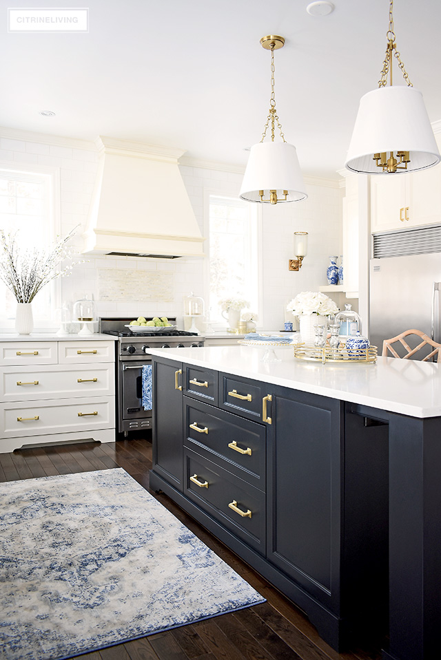Beautiful kitchen with spring decorating - white cupboards, black island and brass hardware create a timeless backdrop. Touches of blue and white and faux flowers are elegant and chic!