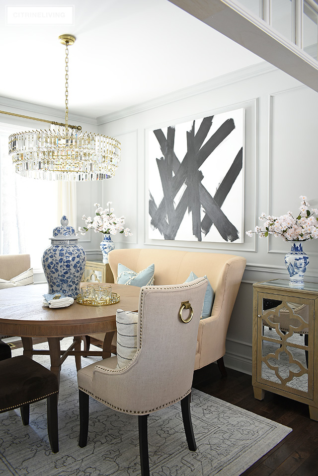 Dining room featuring modern, abstract art, grey walls, moldings, crystal chandelier. Simpler spring decorating with blue and white chinoiserie and faux cherry blossoms.