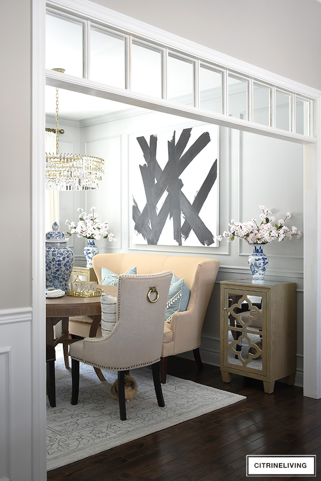 Dining room featuring transom details, modern abstract art, grey walls, moldings, crystal chandelier. Simple spring decorating with blue and white chinoiserie and faux cherry blossoms.
