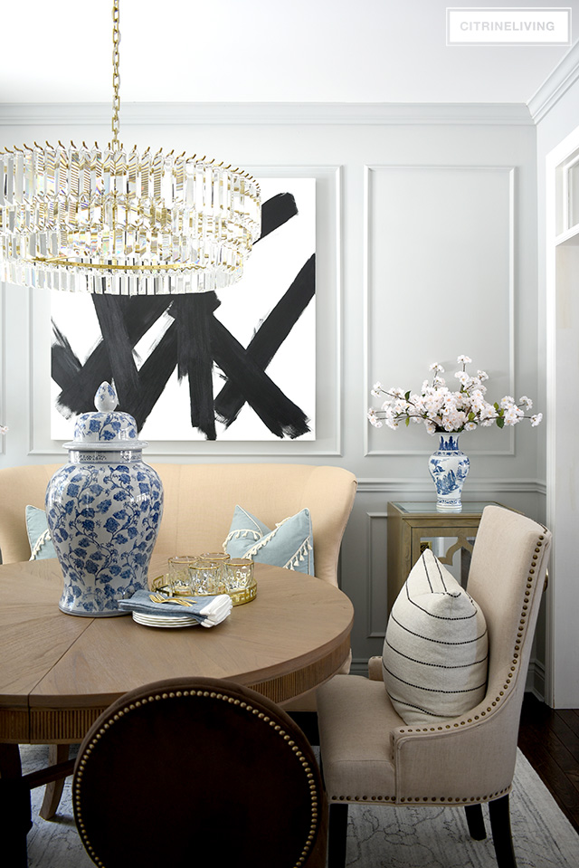 Dining room with large crystal chandelier, modern abstract art, wall moldings, blue and white spring decor and faux cherry blossoms.