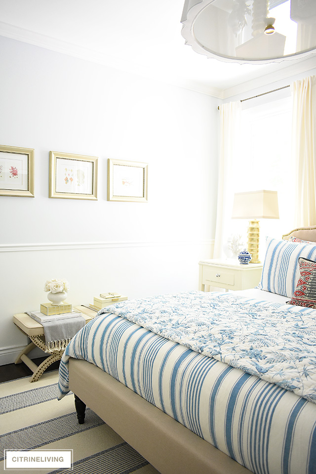 Elegant summer decorated bedroom with ivory and brass accessories, blue and white bedding.