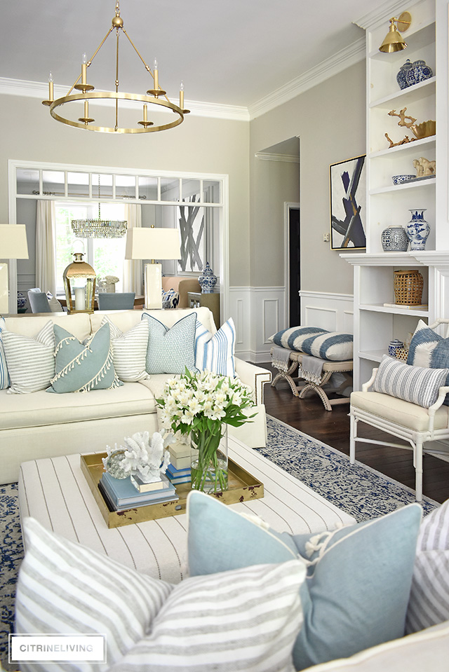 Living room with white sofas and accent chairs, layers of pillows with stripes and light blue hues for an airy coastal chic look.