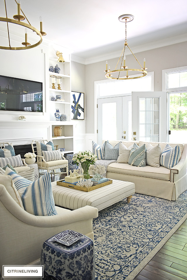 Summer decorated living room with blue and white, brass and stripes. Layered pillows in mixed patterns for a relaxed, coastal feel.