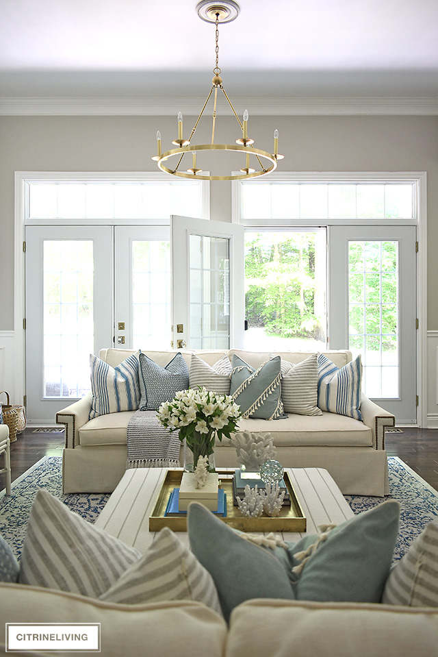 Elegant and chic summer decorated living room with light blue, white, and stripes, coral sculptures and brass accents.