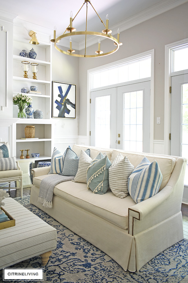 Coastal chic living room with elegant white sofa, layered pillows in soft blue hues and mixed patterns for a chic beach look.