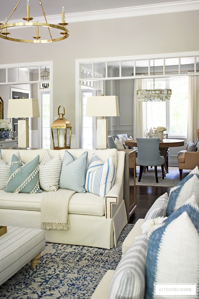 Open concept living room decorated fir summer with light blue, white, creams, ivories featuring pillows with stripes and mixed patterns.