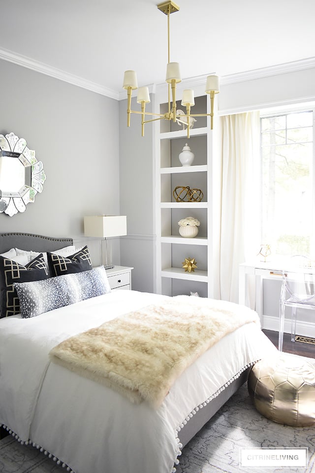 A fabulous fashion-forward teen girl bedroom makeover with chic and elegant details - grey upholstered bed with brass nailhead trim, soft layers of pompom bedding with added texture and pattern and a chic brass chandelier to complete the look! 