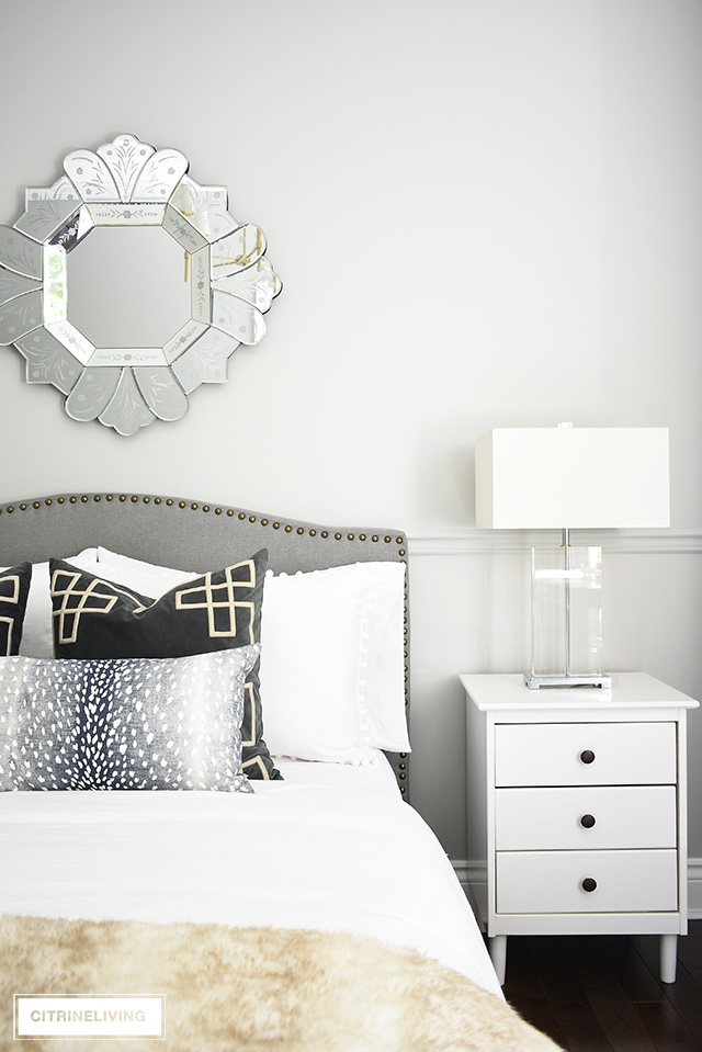 Gorgeous teen girl bedroom makeover featuring a beautiful and tailored grey upholstered bed with brass nailhead trim, venetian style mirror and glam crystal table lamps. Layers of pattern and textured on the upholstered bed are fashion-forward and chic!