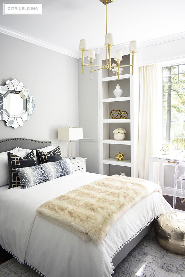 A fabulous fashion-forward teen girl bedroom makeover with chic and elegant details - grey upholstered bed with brass nailhead trim, soft layers of pompom bedding with added texture and pattern and a chic brass chandelier to complete the look! 