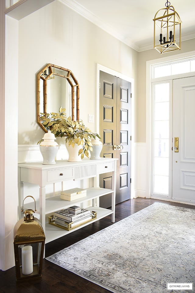 Console table styled with elegant fall decor. Ginger jars, faux gold leaves, gold/lucite tray, design books.