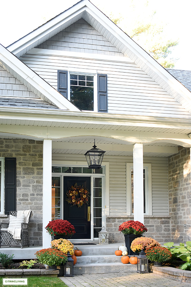 Beautiful fall front porch with gorgeous wreath, colourful mums and scattered pumpkins creates a warm and welcoming entry for your guests.