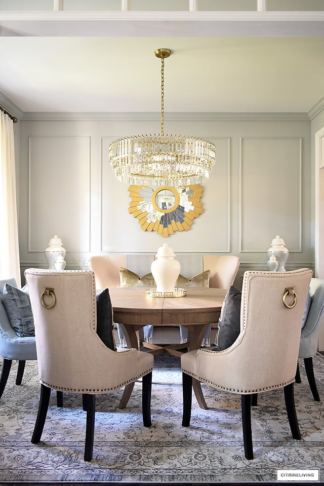 Elegant dining room decorating with classic elements - crystal chandelier, gold sunburst mirror, vintage style rug and classic ginger jars.