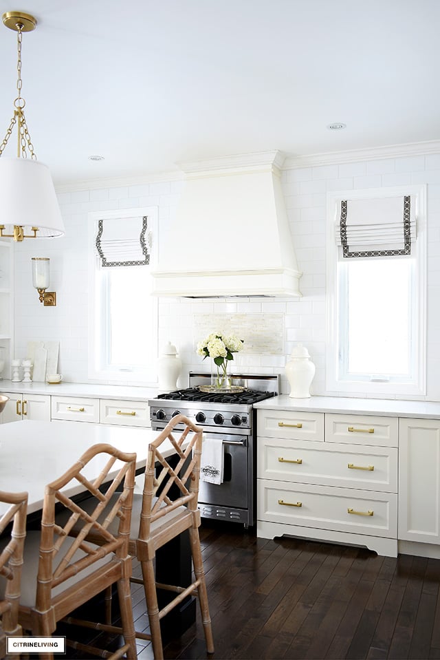 White kitchen with windows flanking the custom range hood, roman shades with ribbon detail.