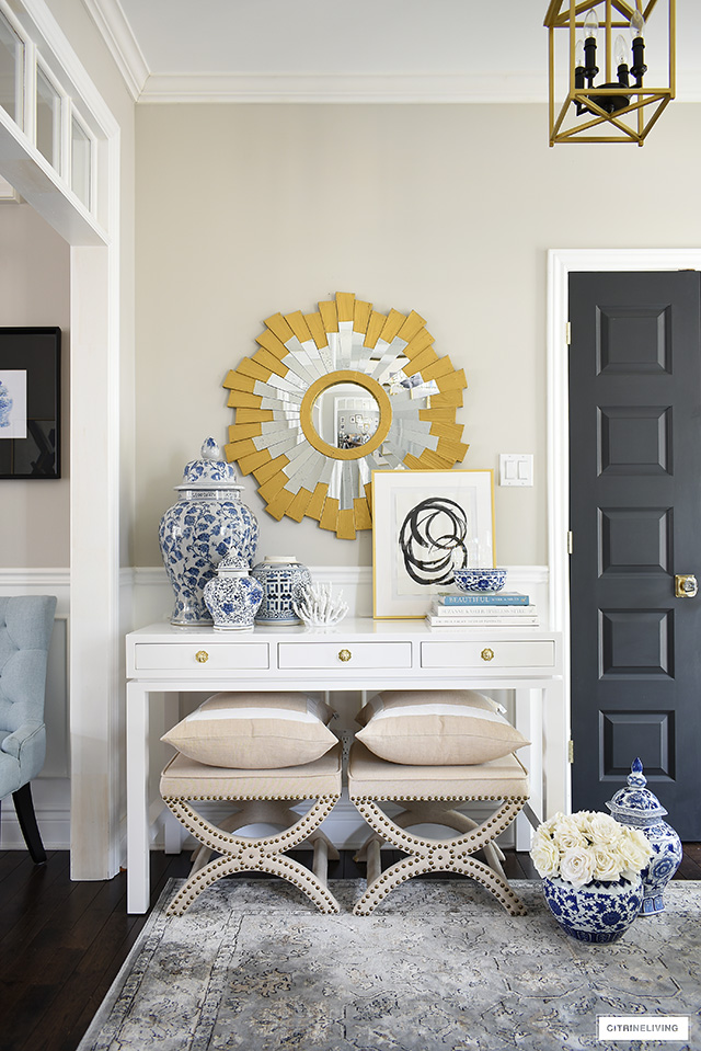 A beautifully styled console table featuring blue and white chinoiserie pieces paired with abstract artwork, design books and a gold sunburst mirror.