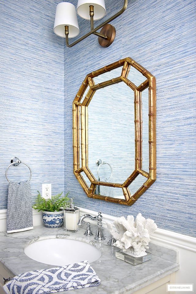 Coastal-chic bathroom with a gold Hollywood regency mirror, vanity with grey marble top and coast accents.