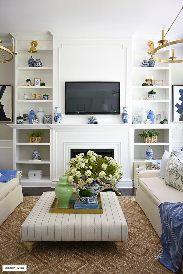 Builtin bookshelves with ginger jars, baskets, greenery, coral gold frame create an elegant curated look in this summer decorated living room.