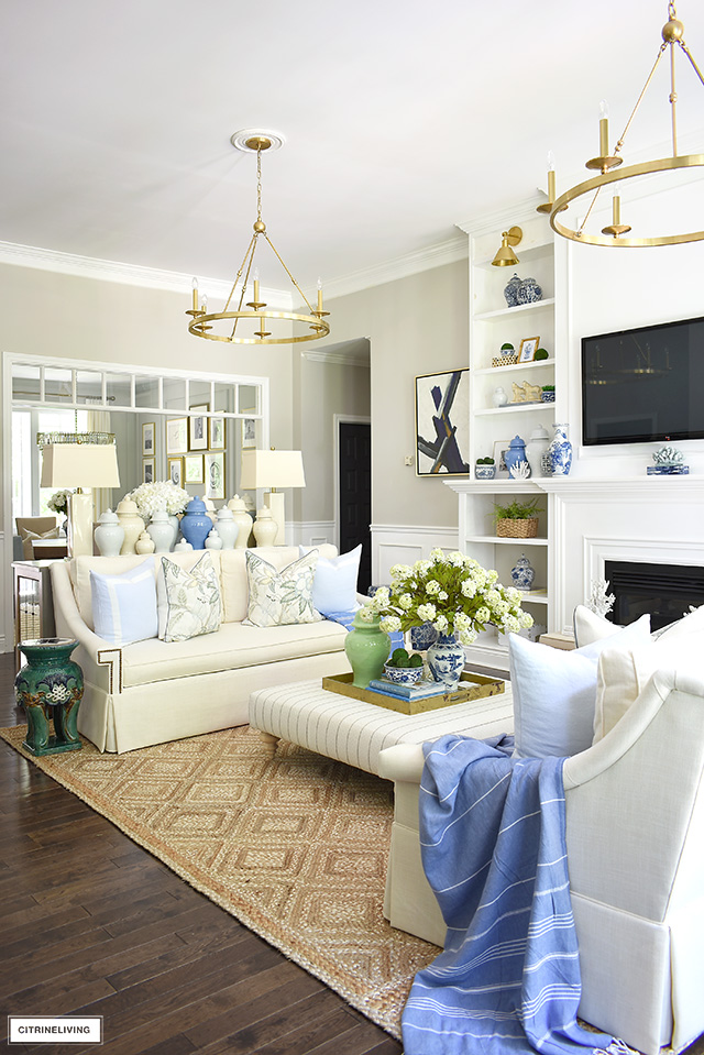 A gorgeous summer decorated living room theme with a natural jute rug, green and blue ginger jars, floral pillows, light blue pillows and greenery accents.