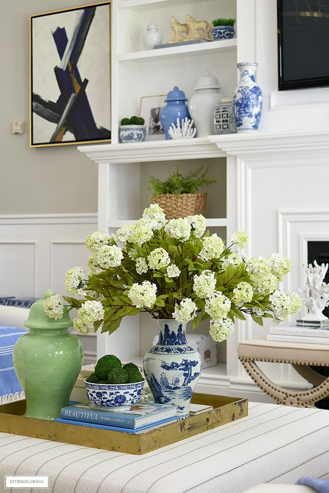 Gorgeous summer ottoman decorating with gold tray, blue and white chinoiserie, green ginger jar, dried moss balls and design books.