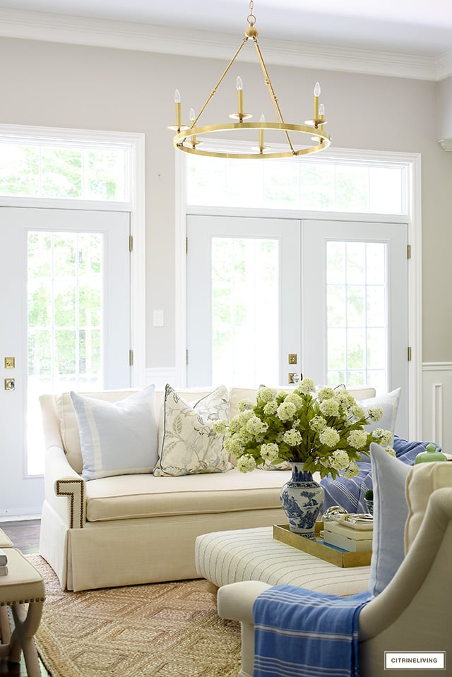 A beautiful summer decorated sofa with light blue pillows, floral pillows, blue throw accented with a jute rug.