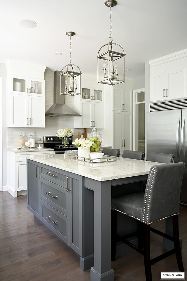 Gorgeous white kitchen with grey island, featuring Satin Nickel handles. Brushed silver pendant lights are elegant and sophisticated!