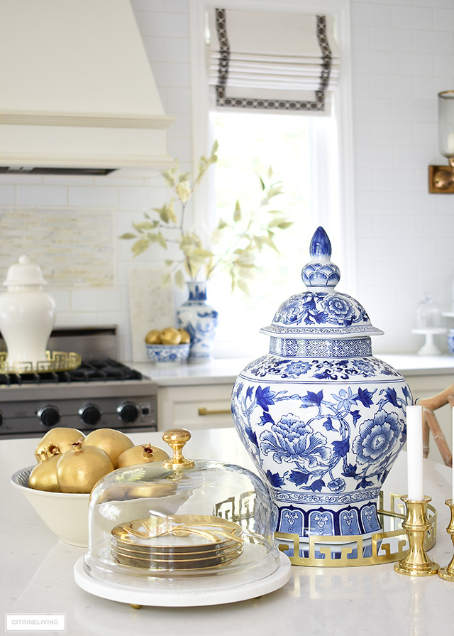 Blue and white ginger jar styled on a kitchen island with gold dishes and gold pomegranates.