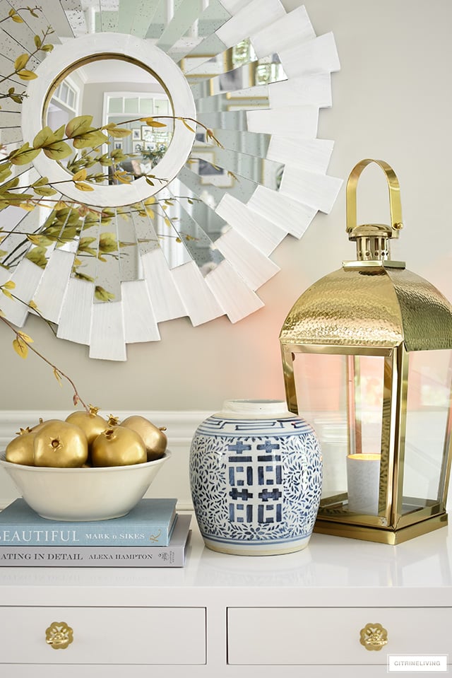 A gorgeous fall display with gold faux fruit, blue and white ginger jar and oversized gold lantern.