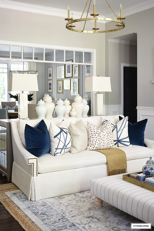 A monochromatic grouping of ginger jars in different sizes arranged behind a sofa on a console table.