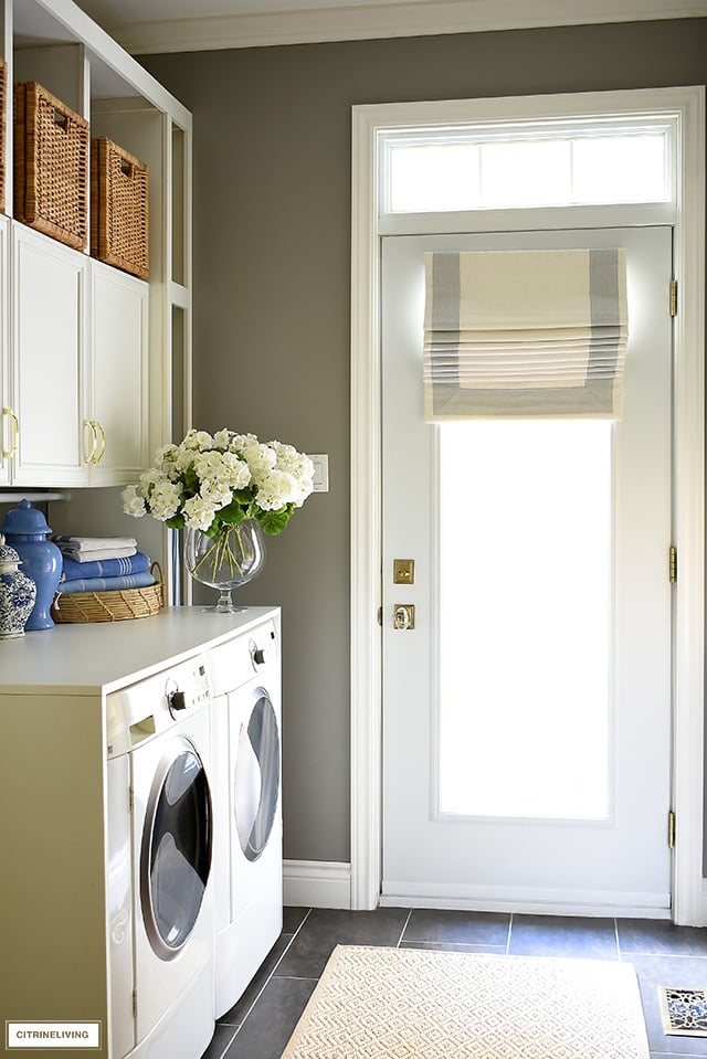 Gorgeous mudroom + laundry room with builtin cabinets, woven baskets and a beautiful custom roman shade.