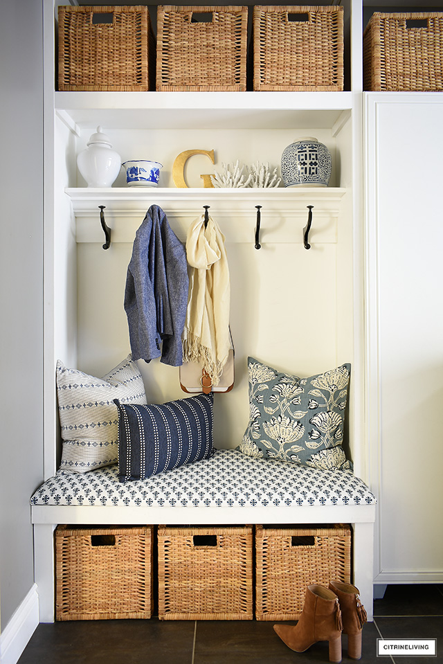 A beautiful builtin upholstered bench with blue and white block print fabric and pillows is a fresh and crisp element in a coastal themed laundry room.