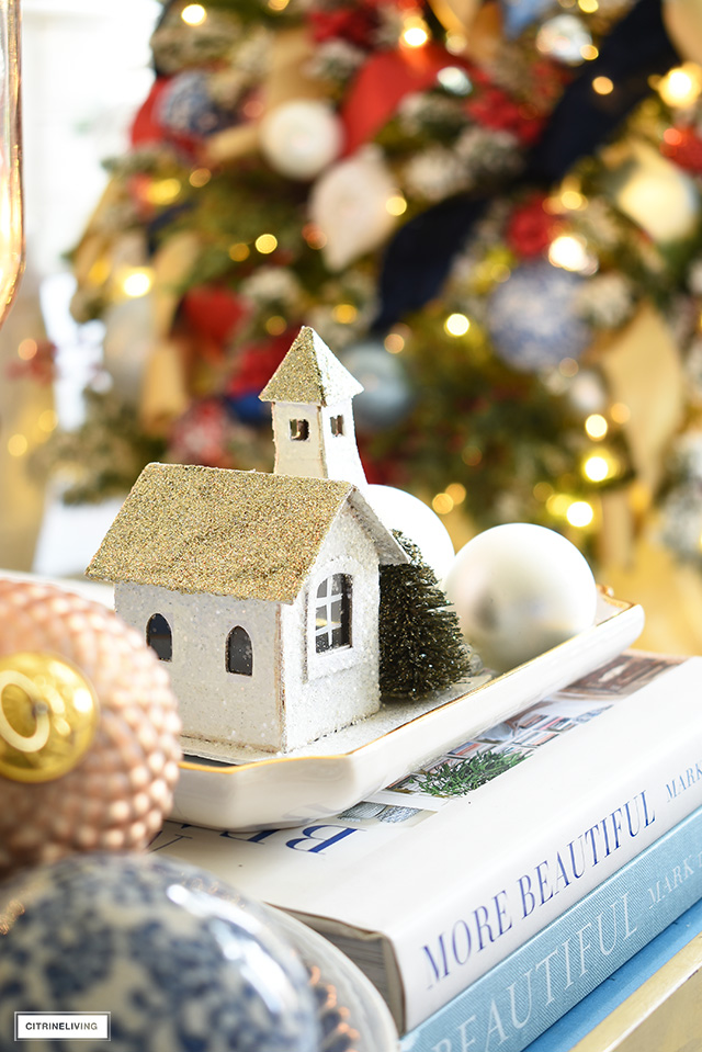 A quaint glittery Christmas house ornament adds a special touch arranged on a small tray with ball ornaments.