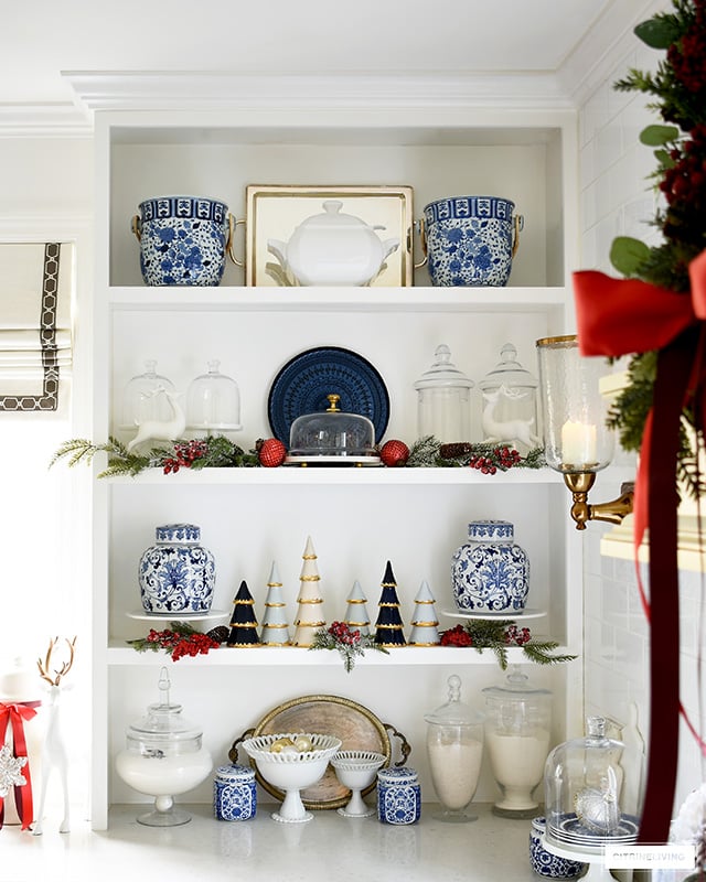 Christmas styled kitchen shelves featuring a gorgeous symmetrical display of blue and white ginger jars, champagne buckets, apothecary jars and holiday greenery with red berries and ornaments.