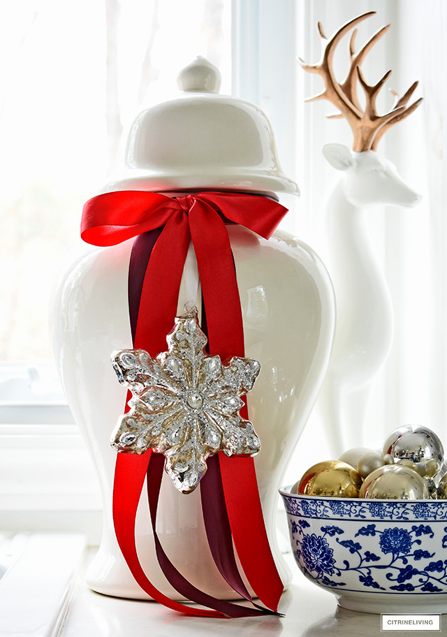 A classic white ginger jar is elevated with beautiful red ribbon and a gorgeous mercury glass snowflake ornament!