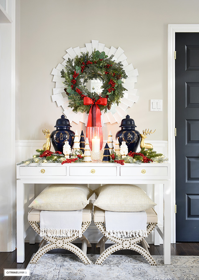 Beautiful white console table decorated for Christmas with ginger jars and Holiday accessories accented with greenery and red berries.