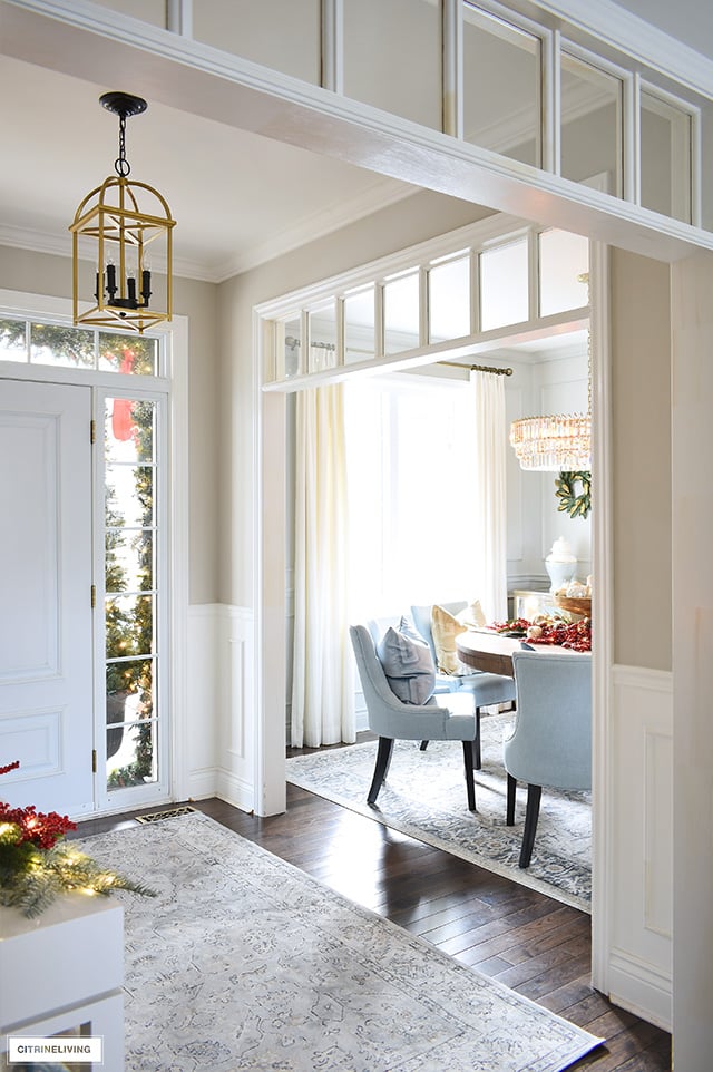 A view into and entryway and dining room space that is open to each other, decorated for Christmas with sophisticated style.