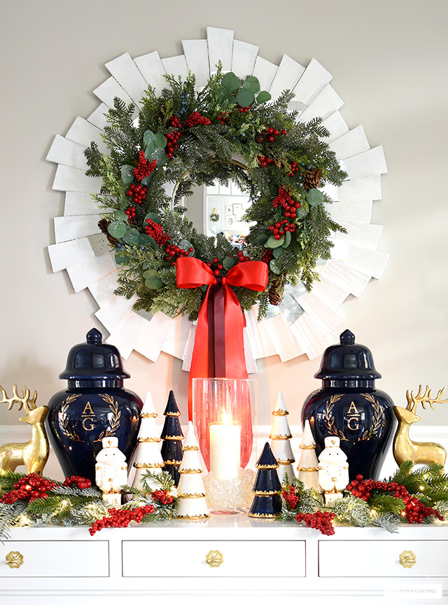 Christmas console table styled elegantly with a symmetrical display of navy and gold monogrammed ginger jars, holiday greenery with red berries.