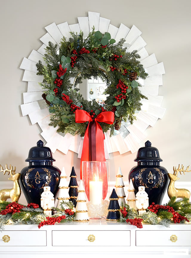 A beautiful green Holiday wreath with red berries and a red bow hung above a console table styled for Christmas.