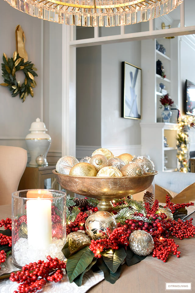 Gold footed decorative bowl filled with silver and gold Christmas ornaments, arranged with a red berry and magnolia centerpiece.