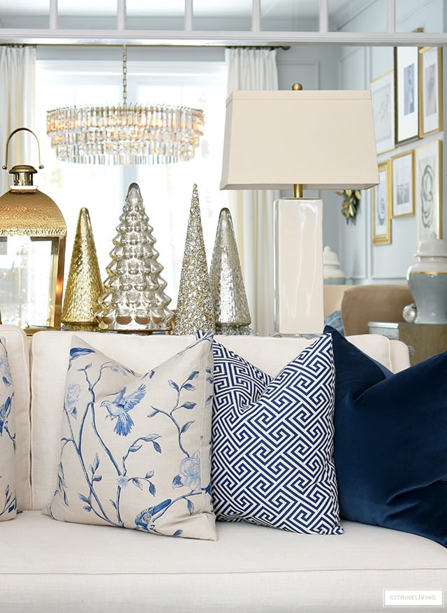 Gorgeous throw pillows styled with mercury glass Christmas trees behind sofa.