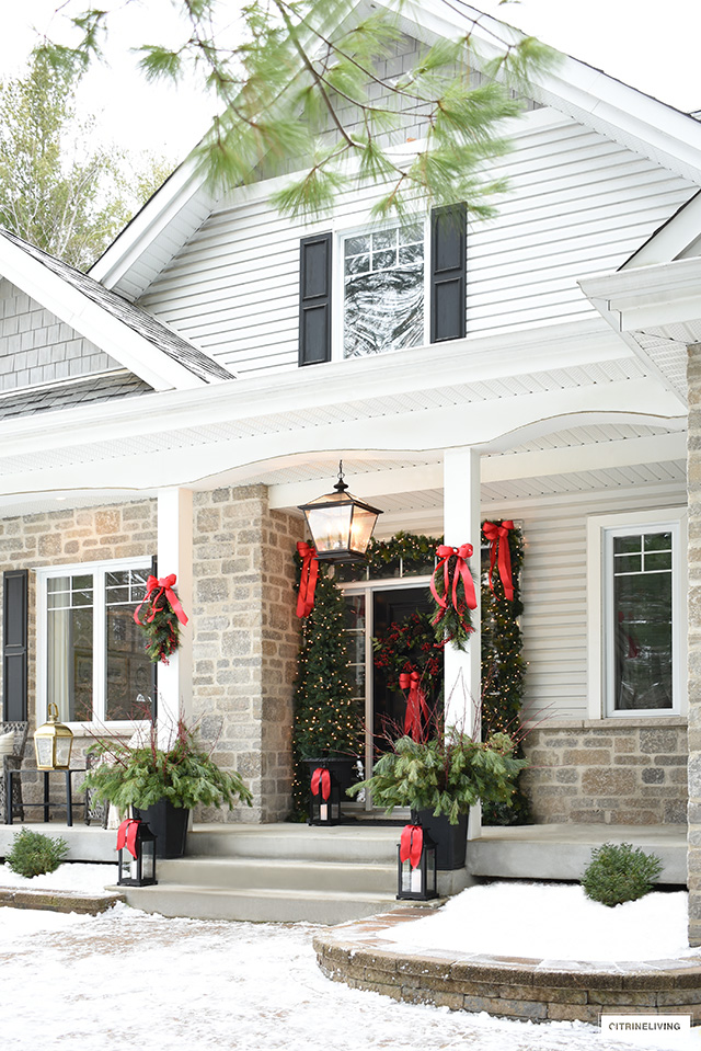 Christmas porch decor with beautiful greenery, red bows and lanterns.