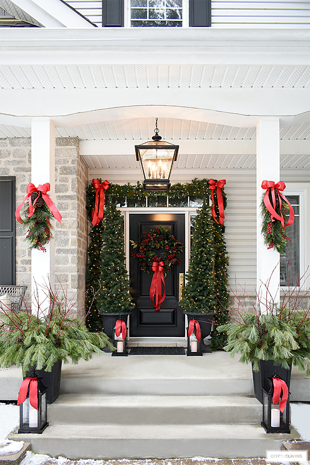 Sophisticated and classic Christmas porch with gorgeous greenery and red bows.