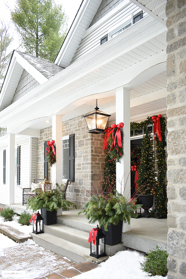 Front porch decorated for the holidays with gorgeous greenery and classic red bows.