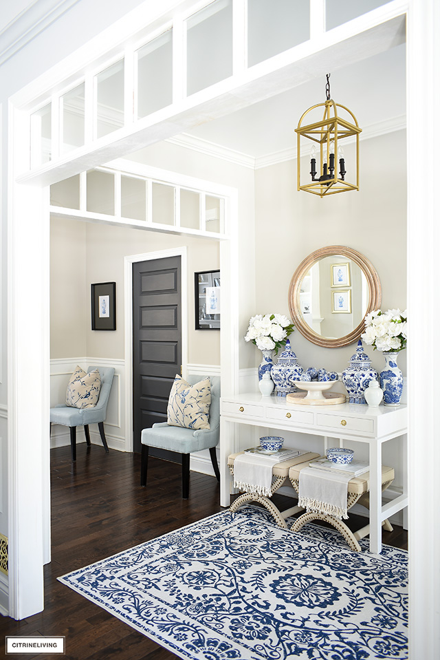 Spring entryway deocrated in layers of blue and white chinoiserie ginger jars, faux peonies and a blue and white print rug.