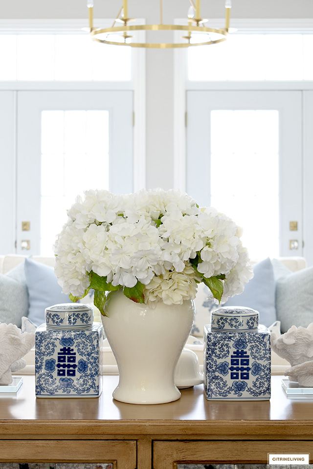 A simple and beautiful living room vignette with white hydrangeas in a white ginger jar, flanked by two identical blue and white square ginger jars.