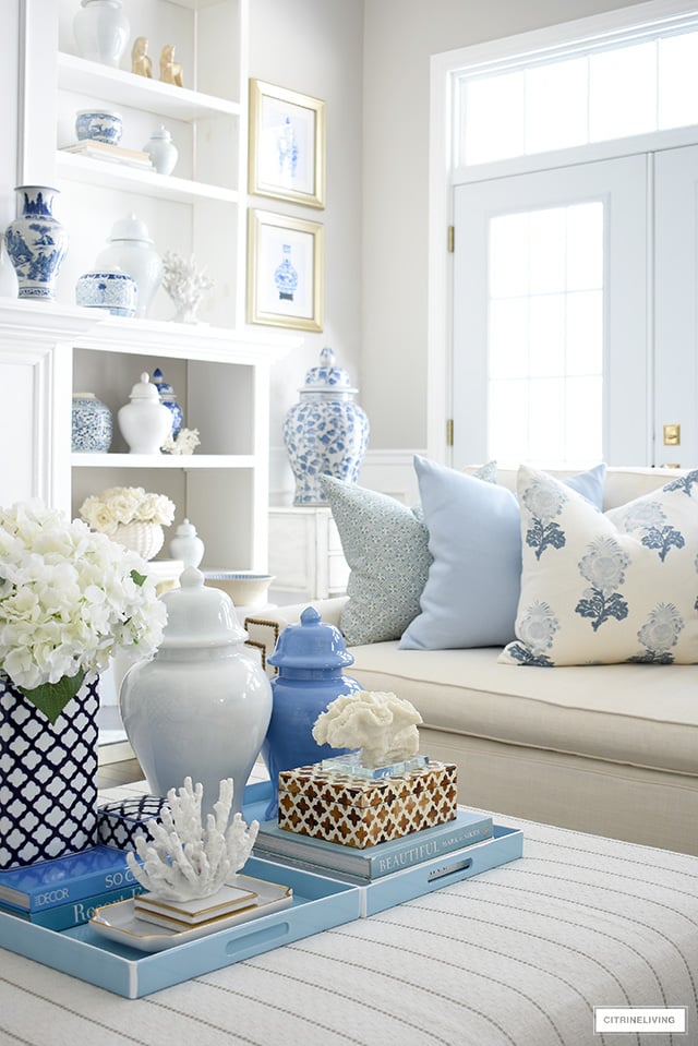 Spring living room decorating - coffee table styled with light blue trays, decorating books, decorative boxes, ginger jars and coral sculptures and faux hydrangeas.