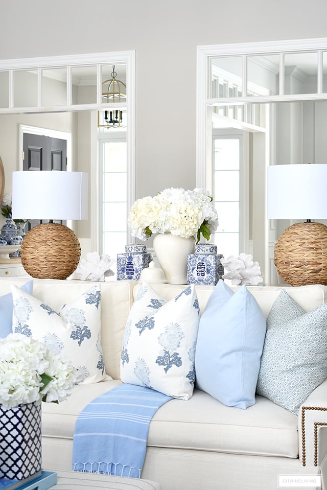 Spring living room decor with beautiful throw pillows in soft blue and white, woven lamps, ginger jars and white florals is elegant and chic.