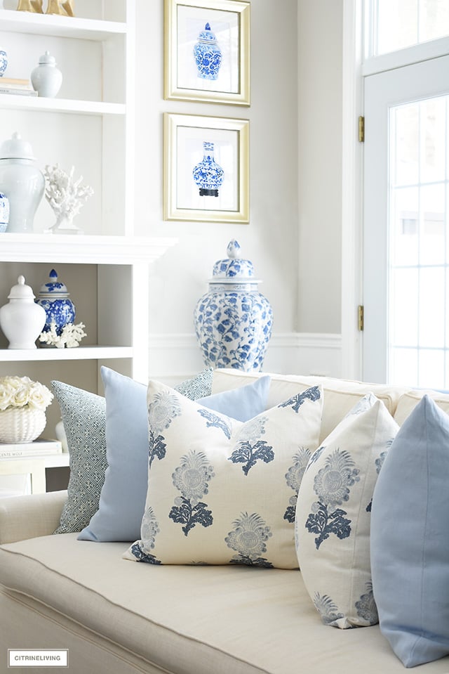 Spring living room decor with gorgeous throw pillows in soft blue and white floral and geometric prints, chinoiserie art prints and ginger jars.