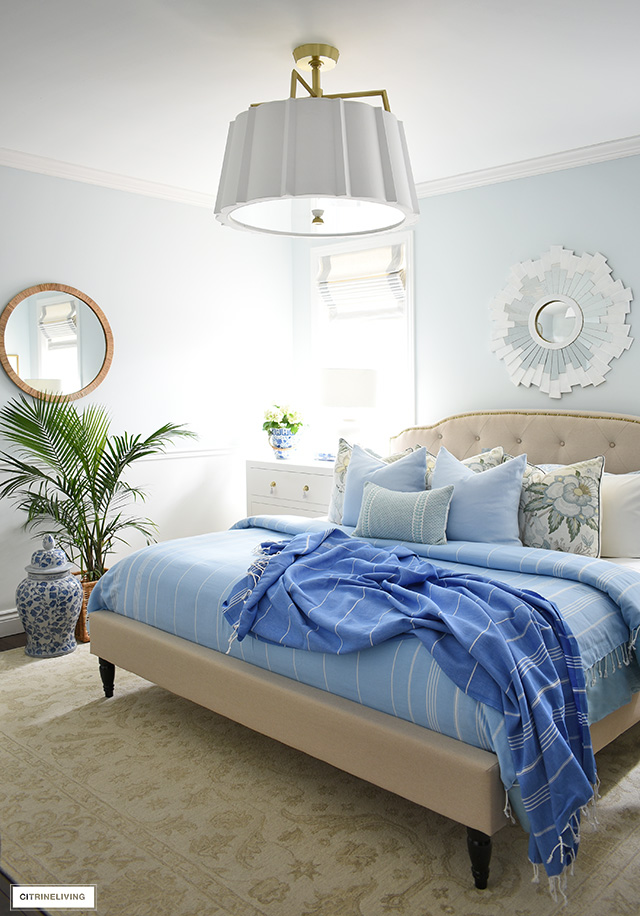 Coastal inspired bedroom styled with palms, ginger jars and striped bedding in layers of blue and white.