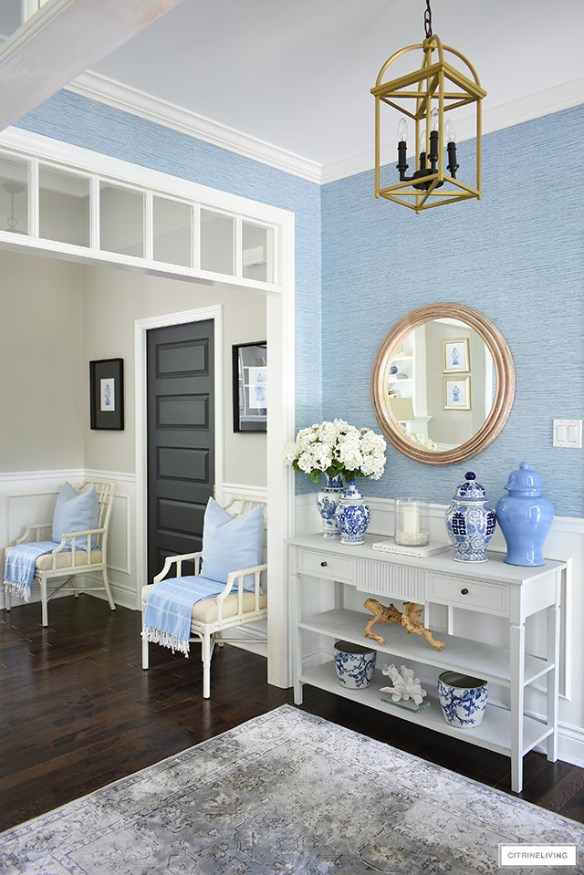 Coastal inspired entryway decorated in blue grasscloth, rattan chairs, natural wood tones and blue and white ginger jars is elegant and sophisticated.