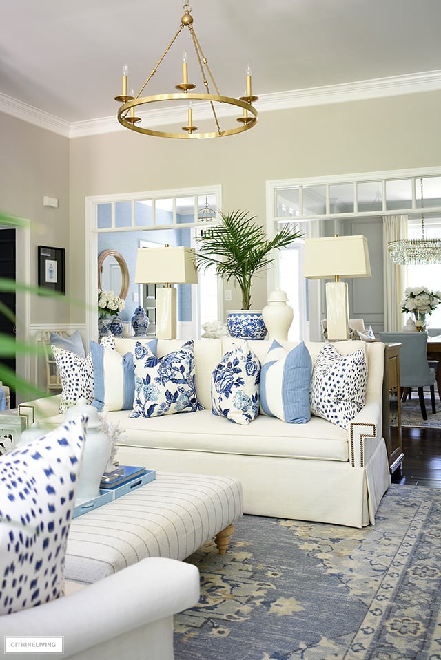 Living room decorated for summer with blue and white pillows and palm plants is an easy way to achieve a coastal look.